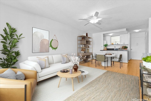 living room featuring ceiling fan, light wood-type flooring, and a textured ceiling