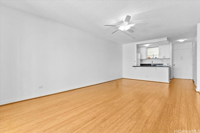 unfurnished living room with ceiling fan, light hardwood / wood-style floors, and a textured ceiling