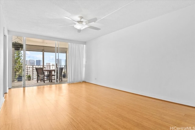 spare room with ceiling fan, floor to ceiling windows, a textured ceiling, and light hardwood / wood-style flooring