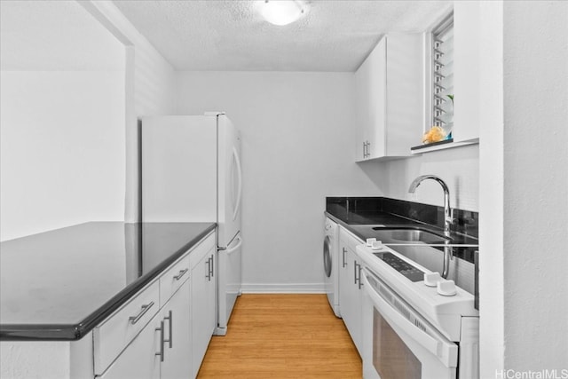 kitchen featuring white appliances, white cabinets, light wood-type flooring, a textured ceiling, and washer / clothes dryer