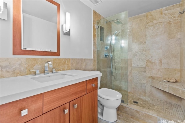 bathroom featuring a tile shower, vanity, tile walls, and toilet