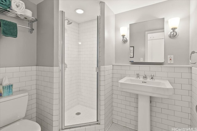 bathroom with a shower with door, toilet, and tile walls