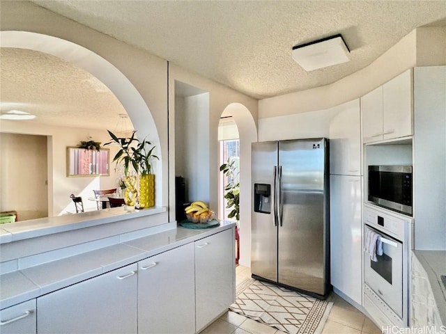 kitchen with white cabinets, appliances with stainless steel finishes, a textured ceiling, and light tile patterned floors