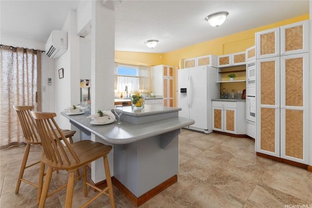 kitchen with a wall mounted air conditioner, a sink, white appliances, a breakfast bar area, and a peninsula