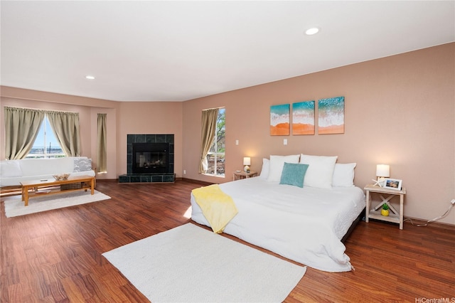 bedroom featuring recessed lighting, wood finished floors, a tiled fireplace, and multiple windows