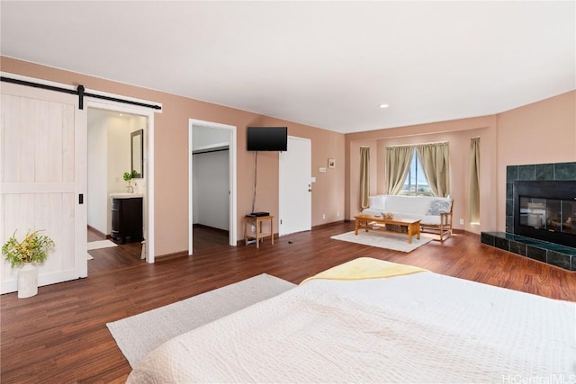 bedroom with a tile fireplace, ensuite bathroom, a barn door, and dark wood-type flooring