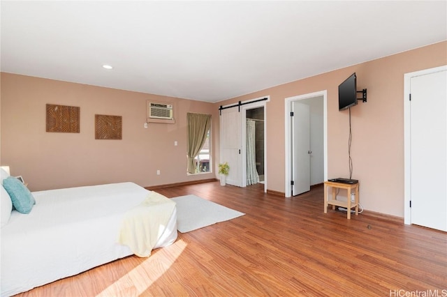 bedroom featuring wood-type flooring, a barn door, and a wall unit AC