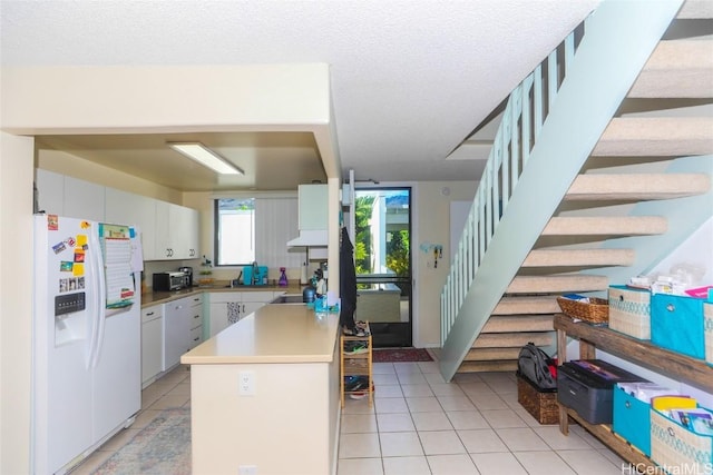 kitchen featuring white refrigerator with ice dispenser, white cabinets, light tile patterned floors, a textured ceiling, and a kitchen island