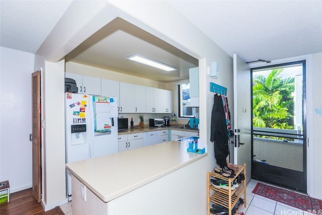 kitchen featuring white cabinets, kitchen peninsula, a textured ceiling, white appliances, and light tile patterned floors