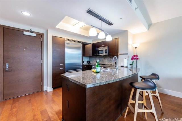 kitchen with dark brown cabinetry, kitchen peninsula, light hardwood / wood-style floors, pendant lighting, and appliances with stainless steel finishes