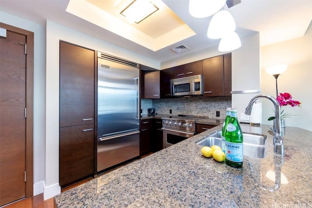 kitchen featuring decorative backsplash, light stone counters, dark brown cabinets, premium appliances, and sink