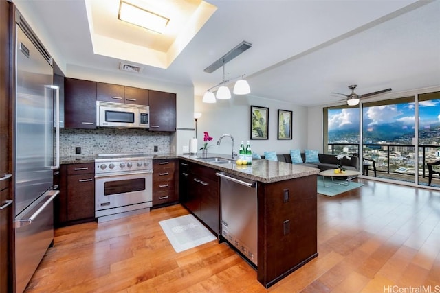 kitchen with high end appliances, sink, decorative light fixtures, light hardwood / wood-style floors, and dark brown cabinetry