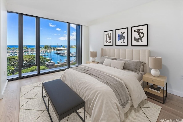 bedroom with a water view, floor to ceiling windows, and light hardwood / wood-style floors