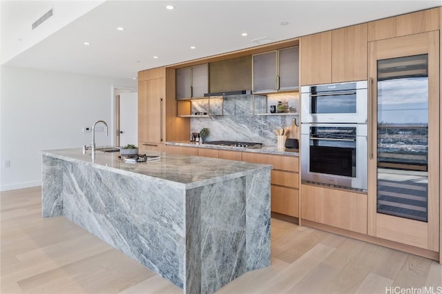 kitchen featuring stainless steel appliances, light stone counters, a spacious island, decorative backsplash, and light wood-type flooring