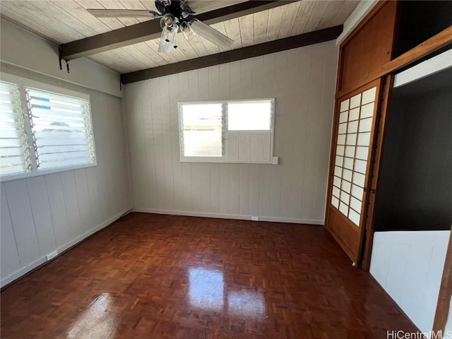 unfurnished room featuring wood walls, plenty of natural light, beamed ceiling, and ceiling fan