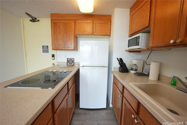 kitchen with a textured ceiling, dark hardwood / wood-style floors, white appliances, and sink