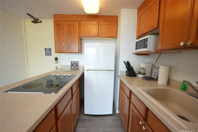 kitchen featuring a textured ceiling, a sink, white appliances, light countertops, and dark wood-type flooring