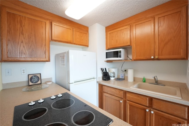 kitchen with brown cabinets, light countertops, a sink, white appliances, and a textured ceiling