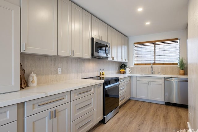 kitchen featuring sink, decorative backsplash, appliances with stainless steel finishes, light hardwood / wood-style floors, and light stone counters