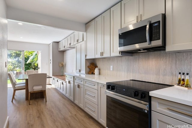 kitchen with range with electric cooktop, light stone counters, decorative backsplash, white cabinets, and light wood-type flooring