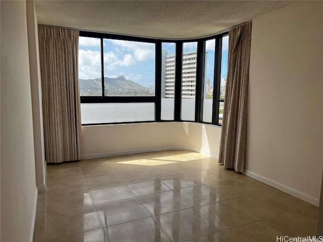 spare room featuring a mountain view, light tile patterned flooring, and a textured ceiling