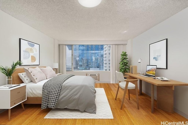 bedroom with an AC wall unit, light hardwood / wood-style flooring, and a textured ceiling