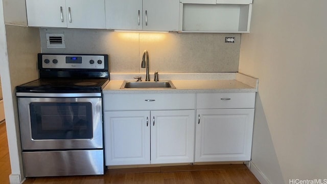 kitchen with stainless steel electric stove, white cabinets, wood-type flooring, and sink