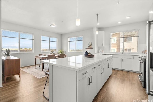 kitchen featuring a kitchen island, stainless steel stove, white cabinets, hanging light fixtures, and hardwood / wood-style flooring