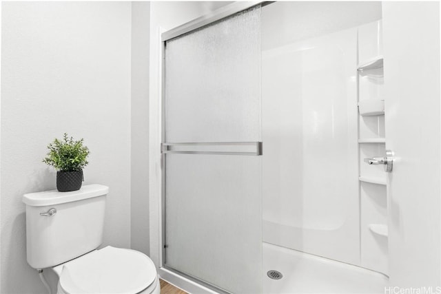 bathroom featuring a shower with shower door and toilet