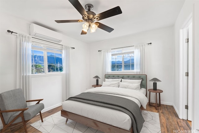 bedroom featuring an AC wall unit, multiple windows, ceiling fan, and light wood-type flooring