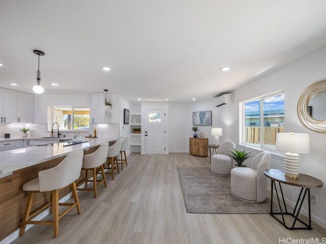 living room with a wall mounted air conditioner, light hardwood / wood-style floors, plenty of natural light, and sink