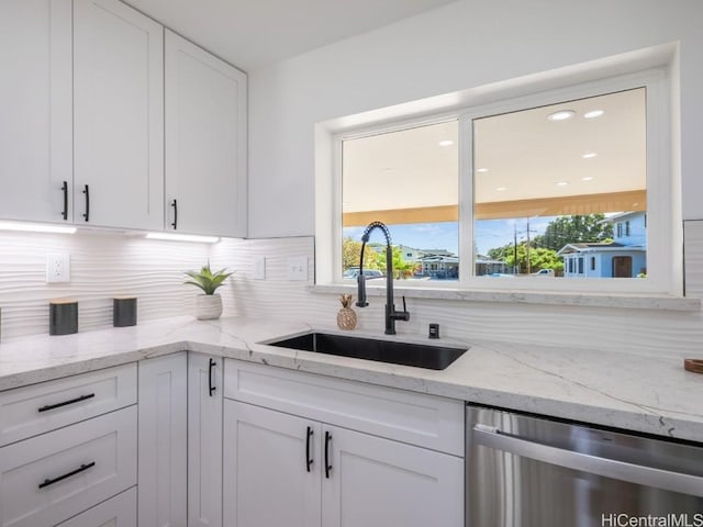 kitchen featuring decorative backsplash, light stone countertops, stainless steel dishwasher, sink, and white cabinets