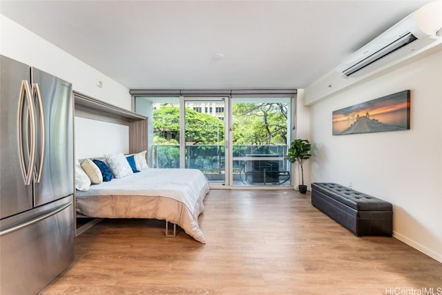 bedroom with stainless steel fridge, light wood-type flooring, expansive windows, and a wall mounted AC