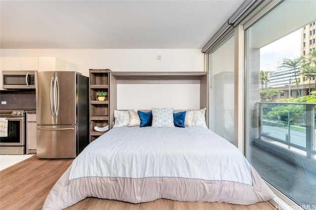 bedroom with access to outside, stainless steel refrigerator, and light hardwood / wood-style floors