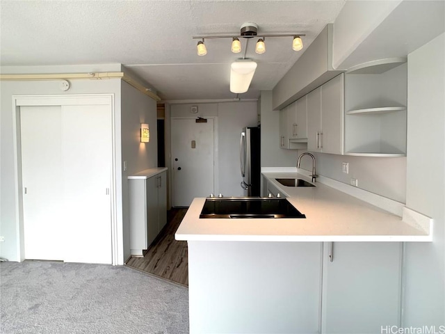 kitchen featuring dark carpet, sink, stainless steel fridge, black electric cooktop, and kitchen peninsula