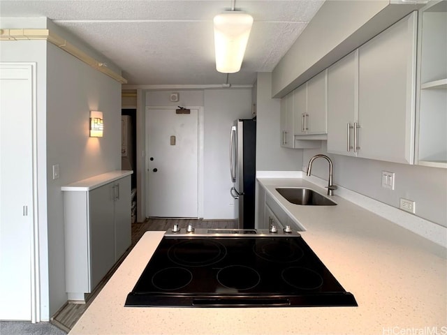 kitchen featuring black electric stovetop, white cabinetry, stainless steel refrigerator, and sink