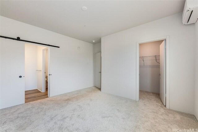 unfurnished bedroom featuring a walk in closet, light colored carpet, a wall mounted AC, a barn door, and a closet