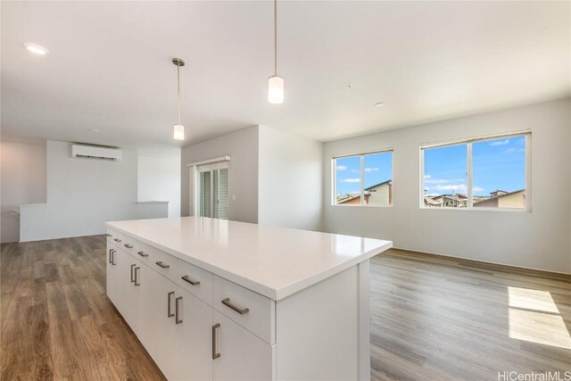 kitchen featuring a center island, a wall mounted air conditioner, wood-type flooring, decorative light fixtures, and white cabinets