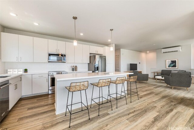 kitchen featuring stainless steel appliances, a wall mounted air conditioner, a kitchen island, light hardwood / wood-style floors, and white cabinets