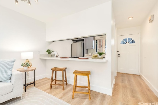 kitchen featuring gray cabinetry, light wood-type flooring, a kitchen bar, kitchen peninsula, and stainless steel refrigerator