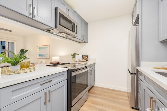 kitchen featuring gray cabinetry, light stone countertops, light hardwood / wood-style flooring, and appliances with stainless steel finishes