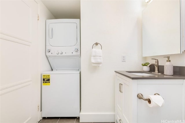 laundry area featuring light tile patterned floors, stacked washing maching and dryer, and sink