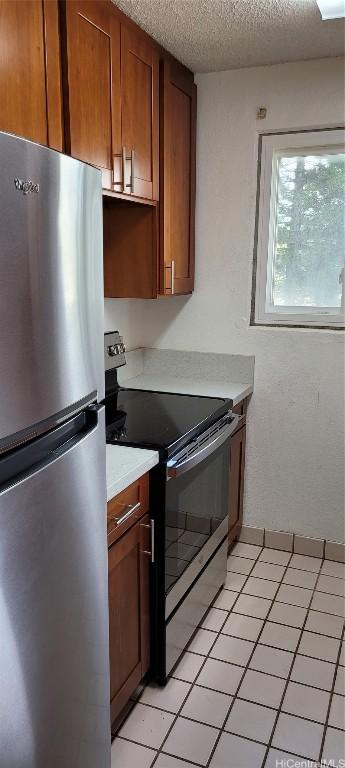 kitchen with light tile patterned floors, a textured ceiling, and appliances with stainless steel finishes