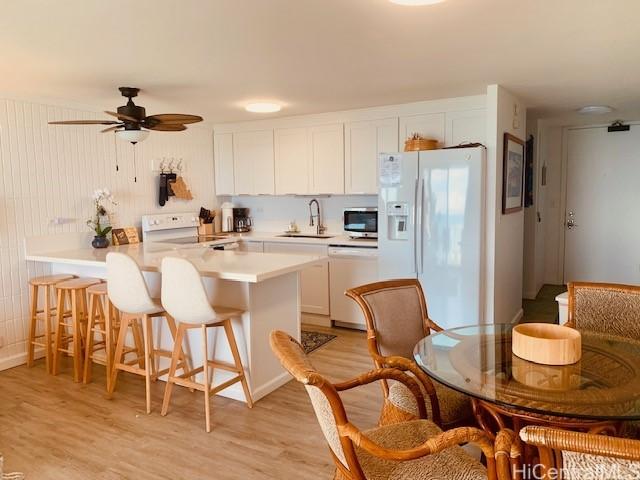 kitchen featuring white cabinetry, sink, a kitchen breakfast bar, light hardwood / wood-style flooring, and white appliances