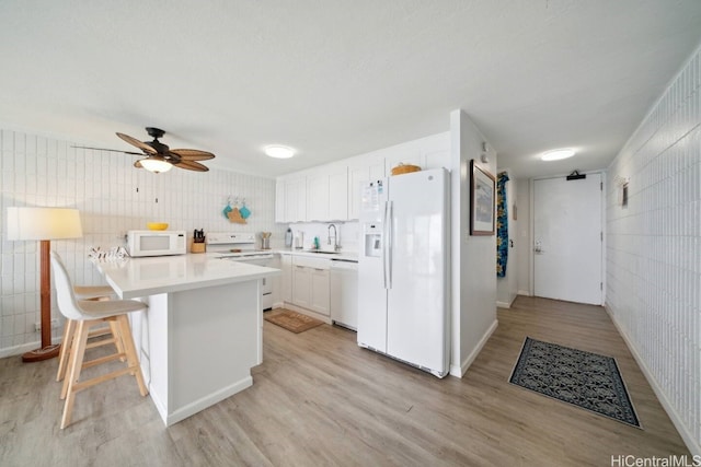 kitchen featuring kitchen peninsula, white appliances, white cabinets, and light hardwood / wood-style flooring