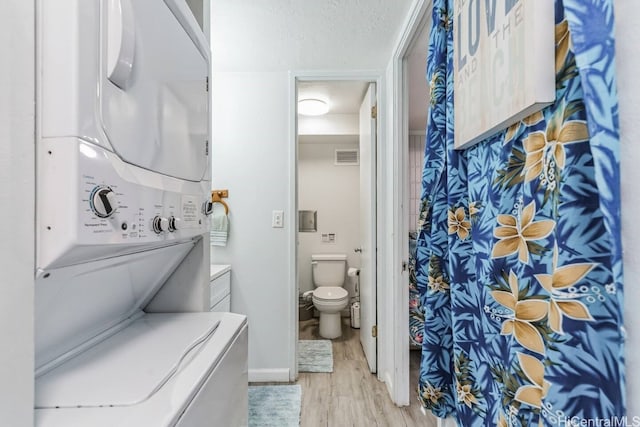 bathroom featuring toilet, wood-type flooring, a textured ceiling, and stacked washer and clothes dryer