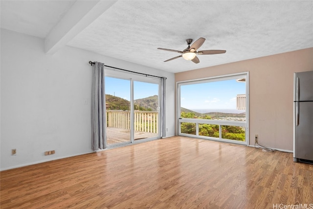 unfurnished room featuring a mountain view, ceiling fan, a textured ceiling, beamed ceiling, and light hardwood / wood-style floors