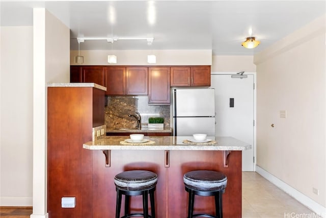 kitchen featuring stainless steel refrigerator, rail lighting, sink, a breakfast bar, and backsplash