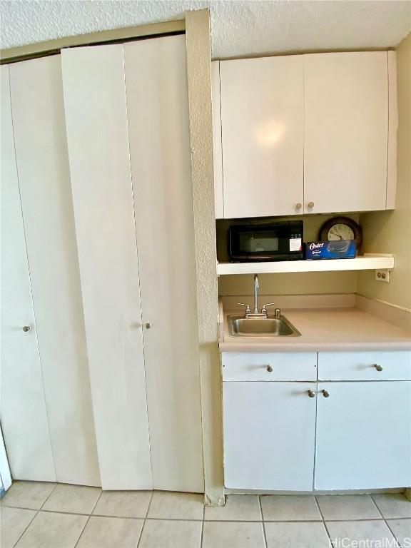 kitchen with white cabinets, light tile patterned flooring, sink, and a textured ceiling