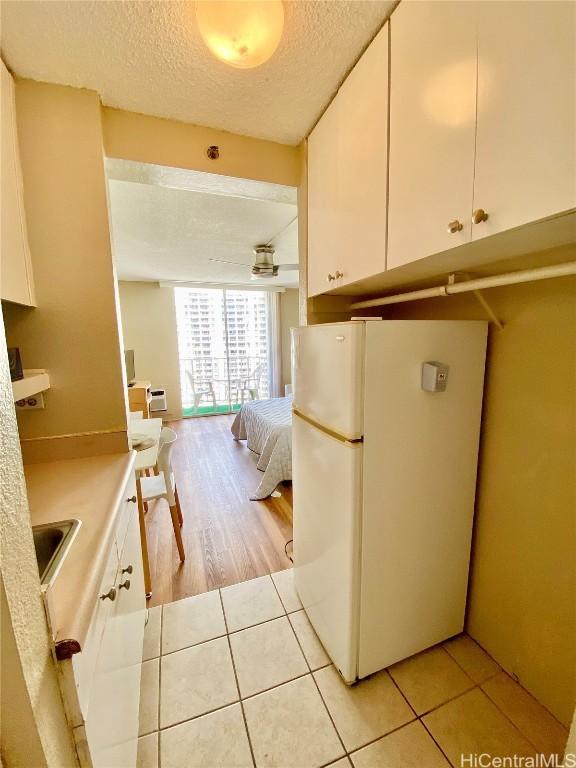 kitchen featuring white cabinetry, light tile patterned flooring, a textured ceiling, and white refrigerator